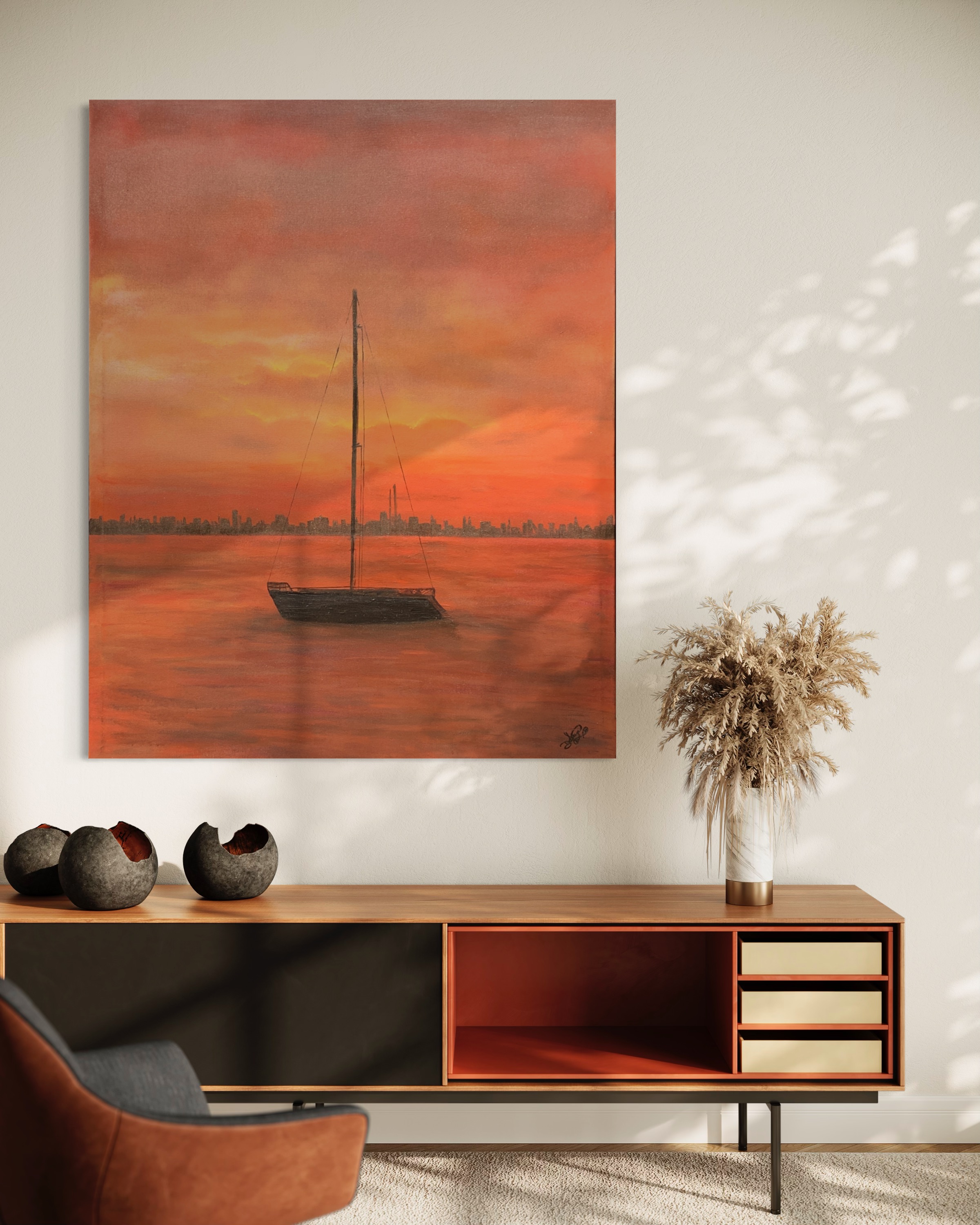An orange sunset and sailboat work presented above a wood console.