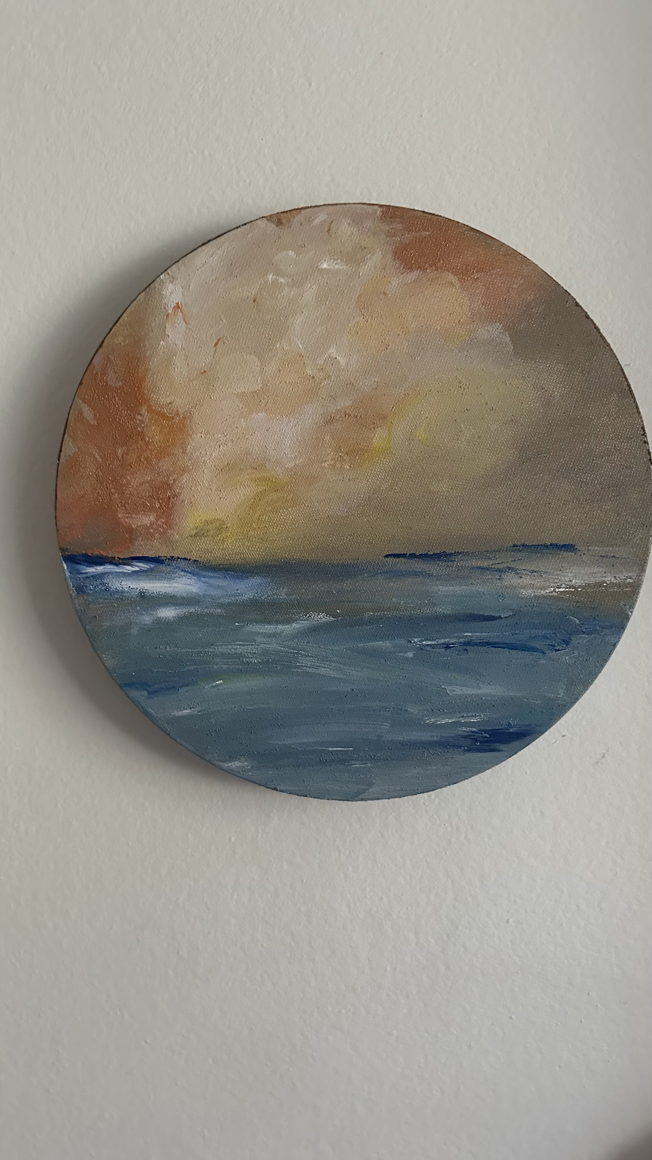 A circular seascape photographed on a wall, with blue water and a softly lit sky.