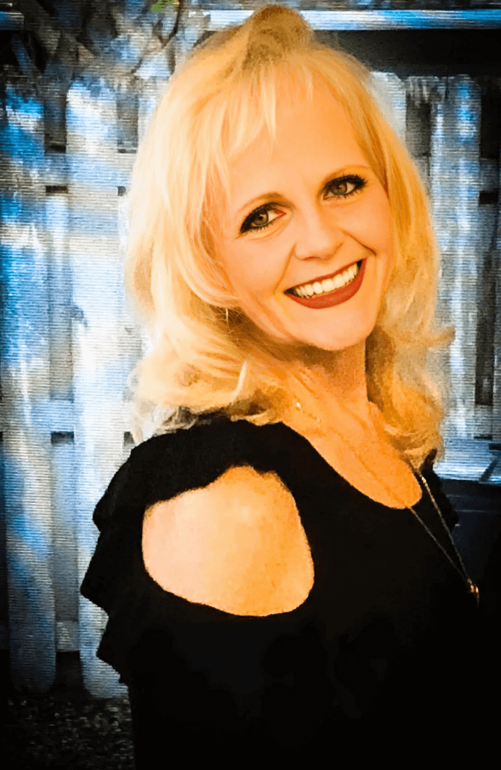 Portrait of artist Danna Donovan, smiling and wearing a black top, with a light background.